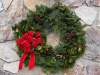 Weihnachtskranz aus Tannenzweigen, Stechpalmzweigen, Zapfen und einer roten Schleife. Im Hintergrund ist eine Steinwand zu sehen.